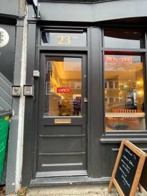 From sidewalk facing venue. Glass door with grey frame. Push to open on right.