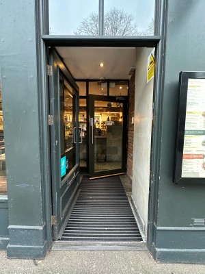 First glass door with grey frame. Push metal handle on right to open.