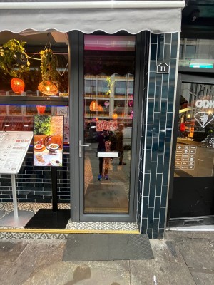 Glass door with grey metal frame. Turn silver handle and push from left.
