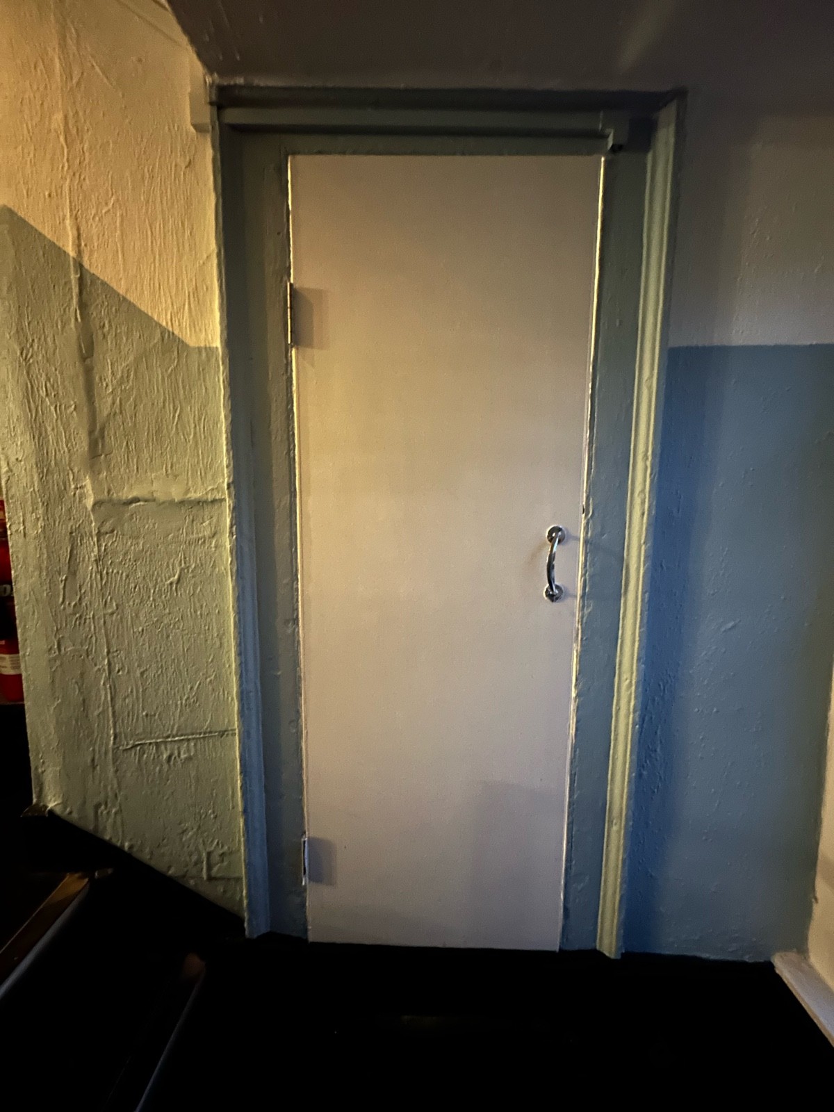 From bottom of steps facing left. White wooden bathroom door ahead. Pull metal handle on right to open.
