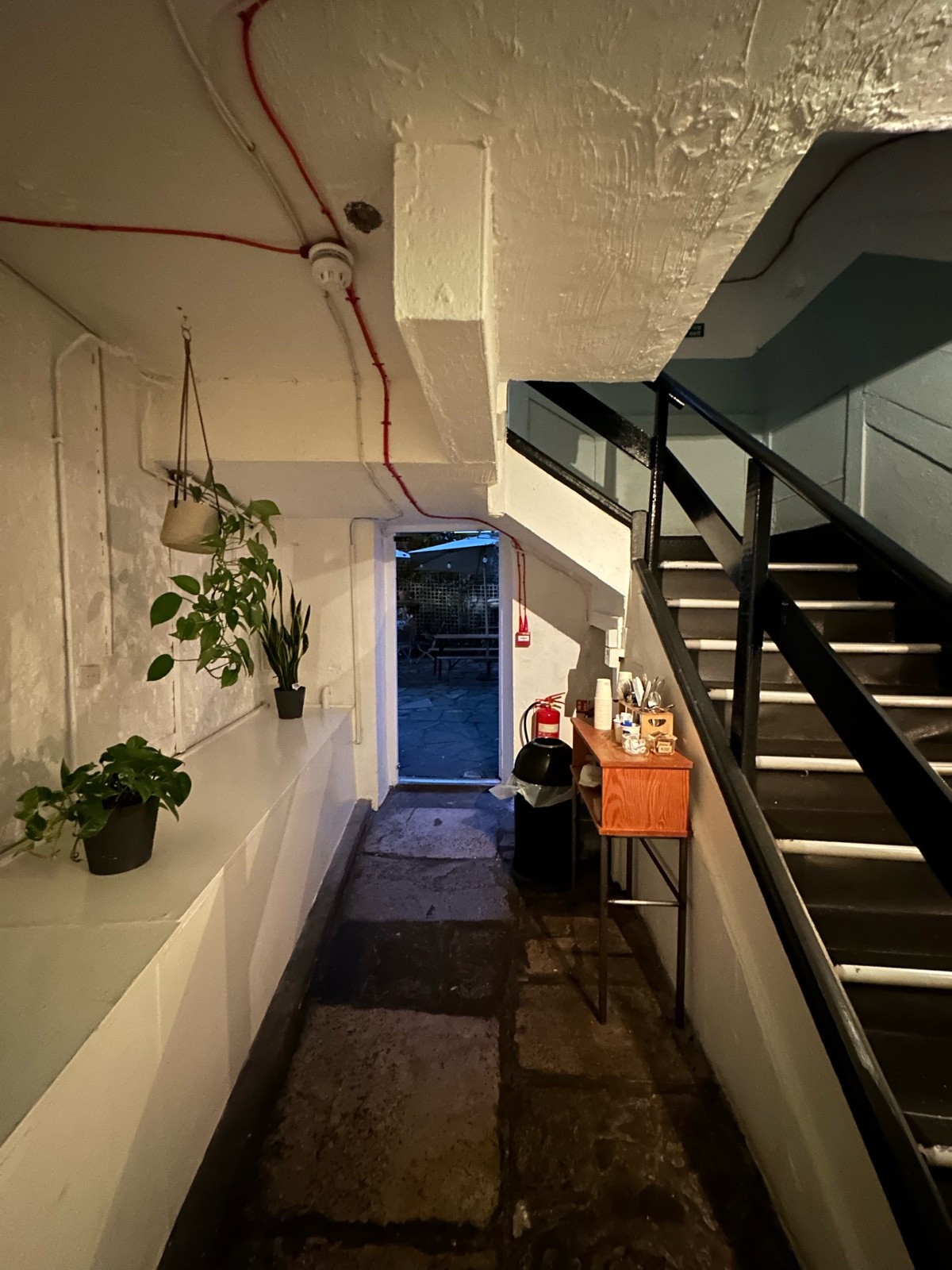 From opening facing right. Display table along left. Path ahead leads to preceding door. Condiments table and bin ahead to right. Stairs behind.