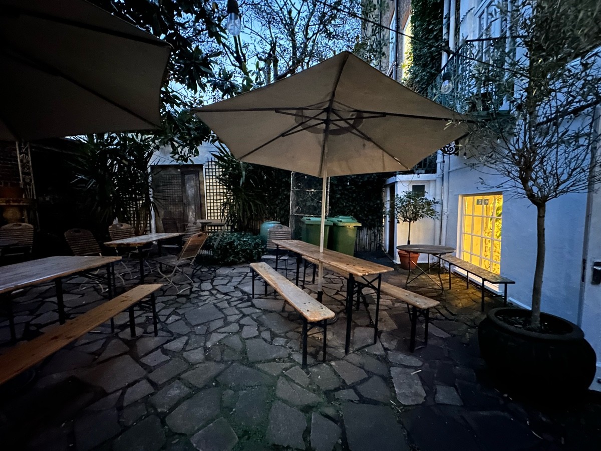 From door facing right. Tables and benches scattered ahead. Plant on right.