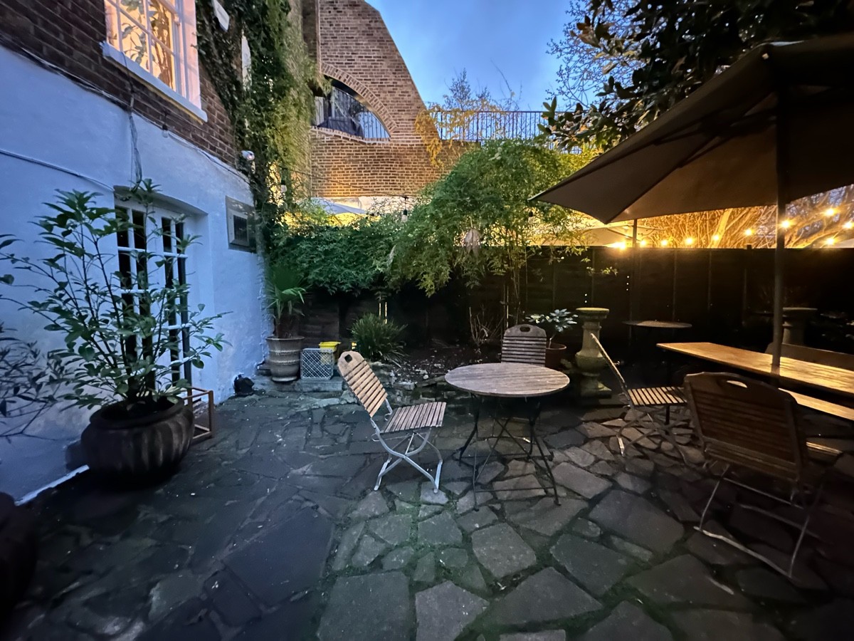 From door facing left. Tables, chairs and benches scattered ahead to right. Plant on left.