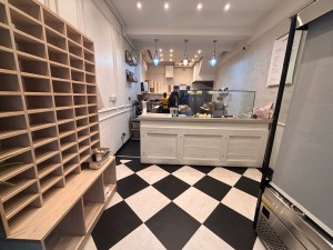 From entrance facing straight. Product shelf at left. Counter at back. Beverage fridge at right.