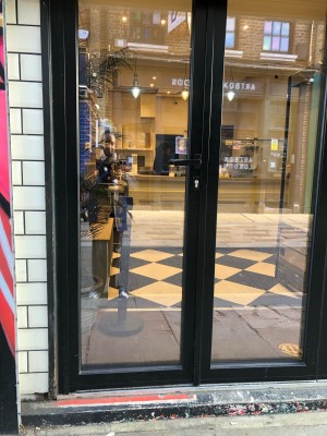 Glass door with black frame. Push handle on right to open.