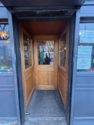 Glass paneled door with wooden grab ahead. Pull metal handle at right to open.