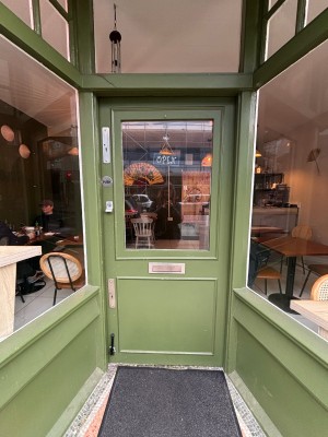 Glass paneled door with green frame ahead. Push at left to open.