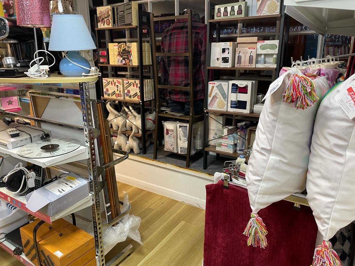 This photo is from the door to the side room facing right. To the right is a rail of textiles, to the left is a rack of bric-a-brac, ahead is a window
