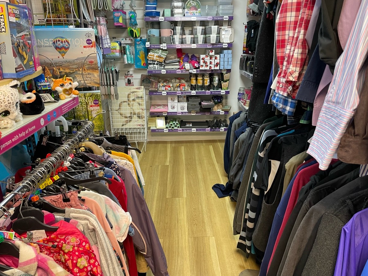 This photo is along the back wall of the side room facing left, to your left is a rack, and the path to the door, to your left is rails of clothes.