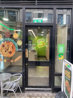 Glass door with black frame ahead. Push door to open via metal handle on left.
