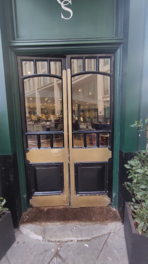 Glass doors with black and gold frames ahead. Push in centre to open.