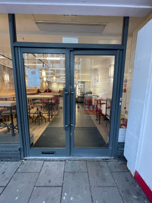 Glass doors with black frame ahead. Black metal handles in centre. Push to open.