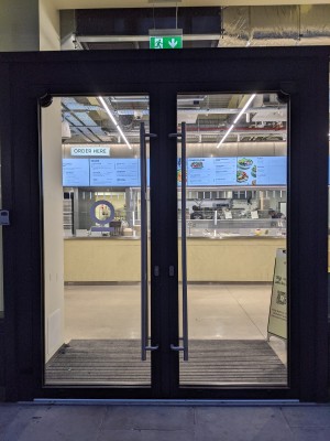 Glass door with grey frame and metal handles. Push from centre to open.
