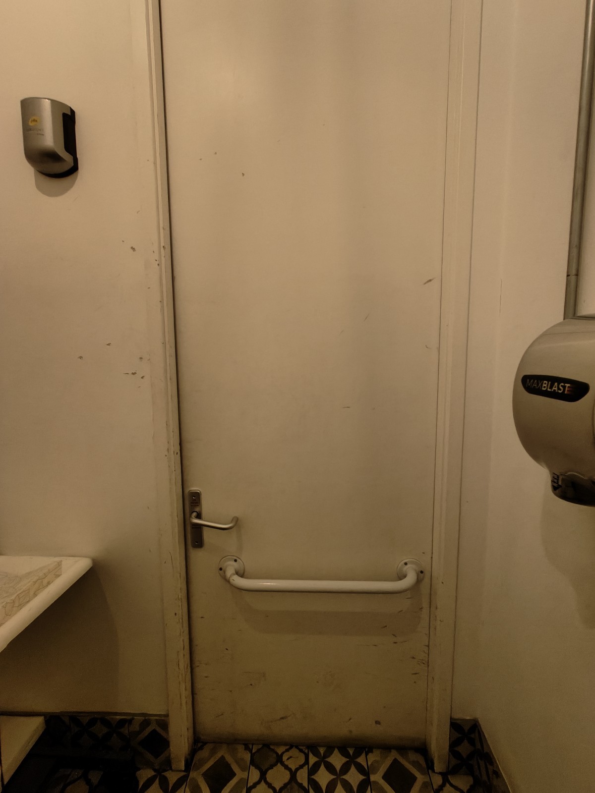 Back of door. White grabrail in centre. Push silver metal handle on left to open.