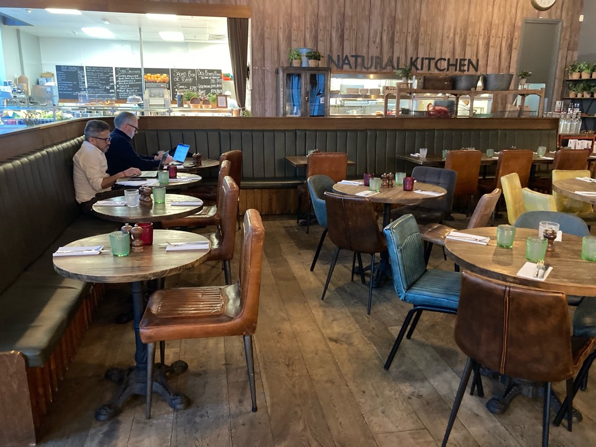 From opening, facing left. Half booth, tables and chairs along left and back. Tables and chairs along right.