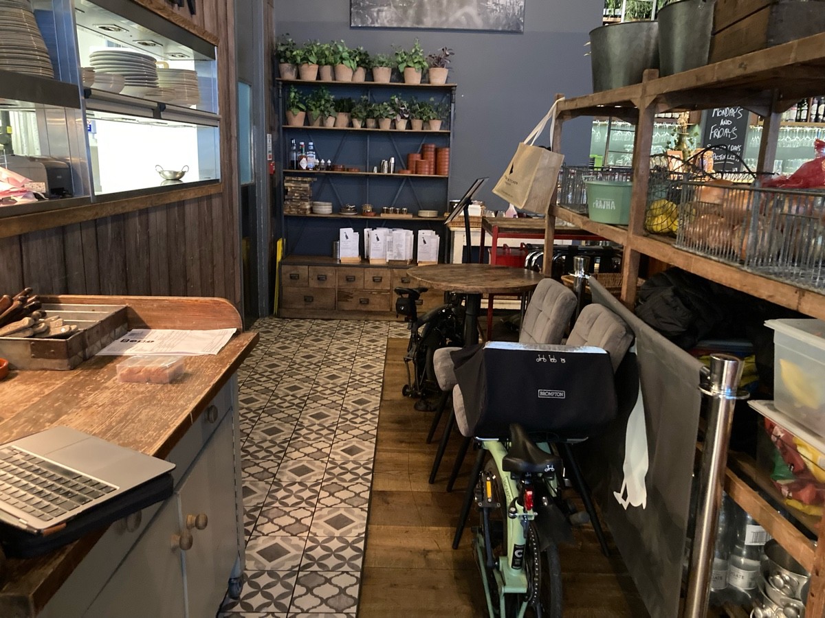 From end of barrier, facing straight. Shelve on right, storage along its left. Shelve on back. Service desk on left, kitchen behind.