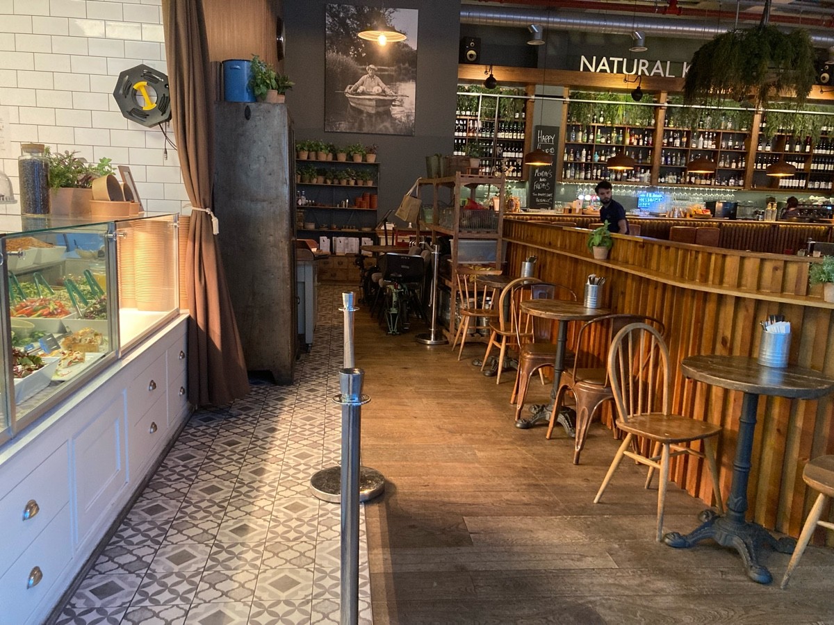 From end of path, facing right. Counter and product display along left. Queue barrier in center. Tables and chairs along divider on right.