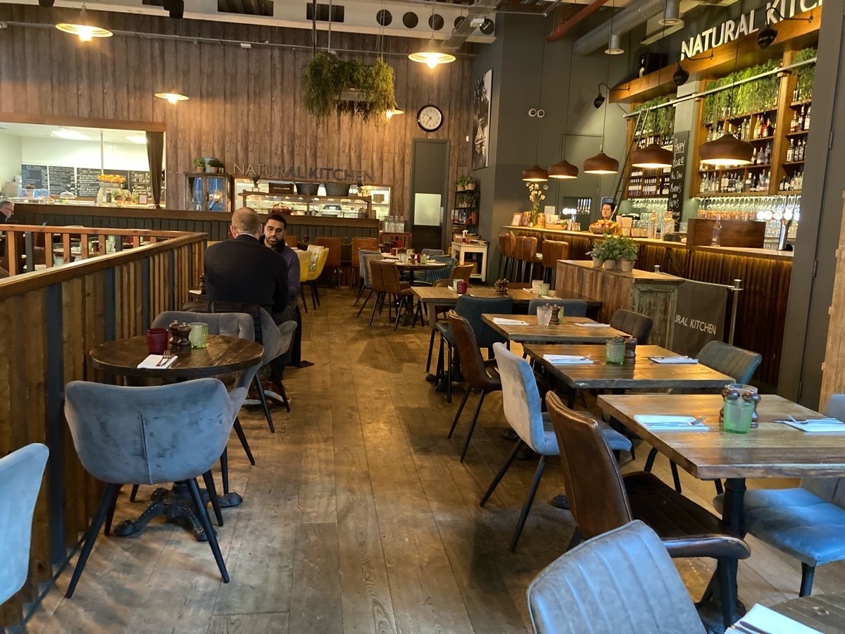 From end of half booth, facing left. Tables and chairs along both sides. Path ahead to bar on back and bathroom on back right.