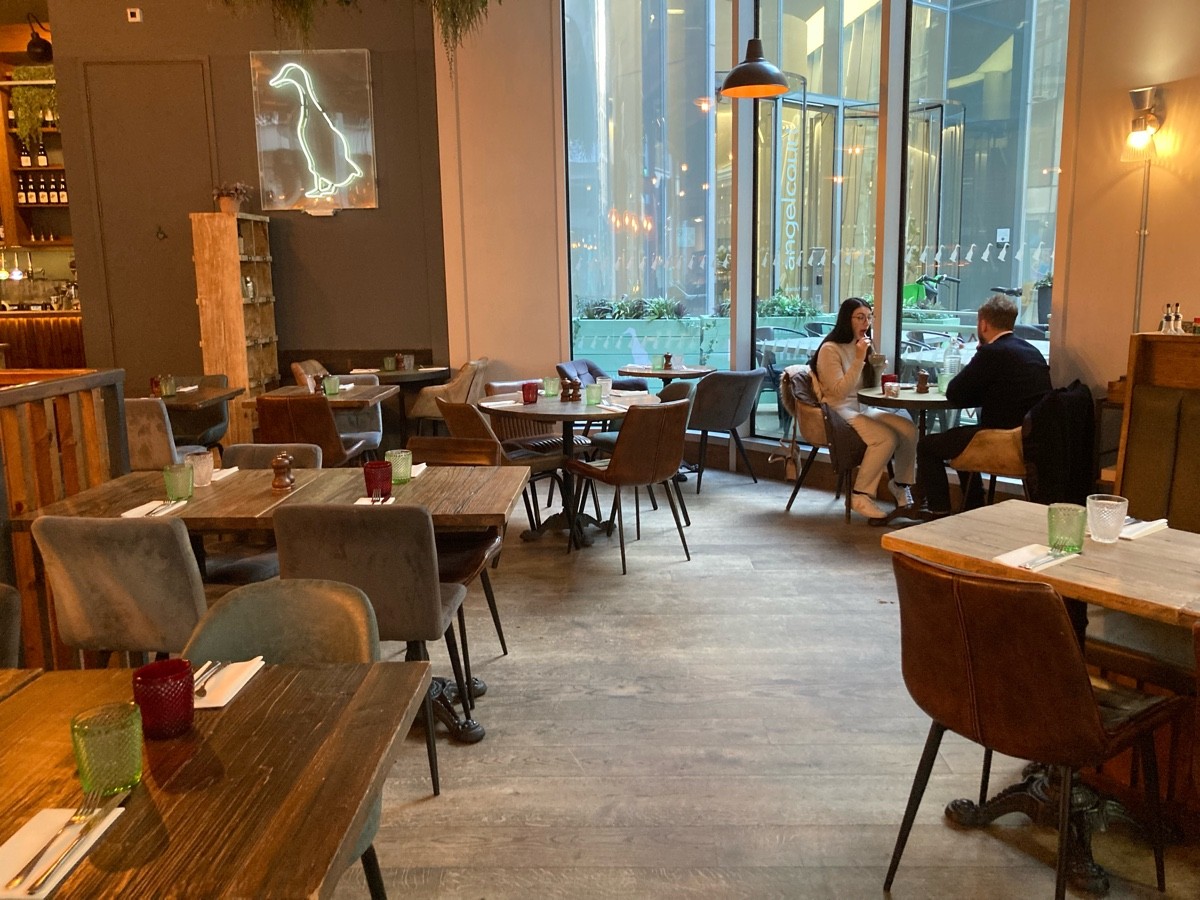 From divider, facing straight. Tables and chairs along left, half booth on right.