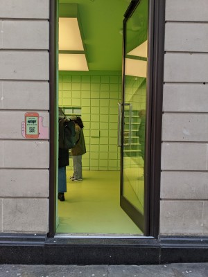 Glass door with black frame and metal handle. Push from left to open.