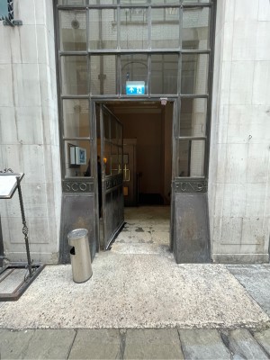From street facing venue. Metal-framed glass door ahead. Push brass handle on right to open.