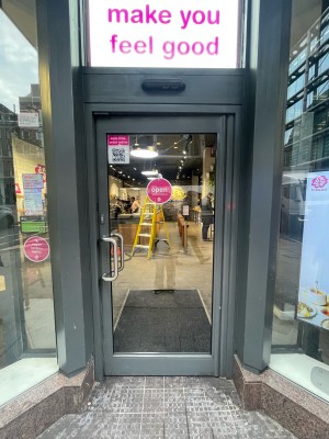 Glass door with grey frame ahead. Push silver metal handle on left to open.