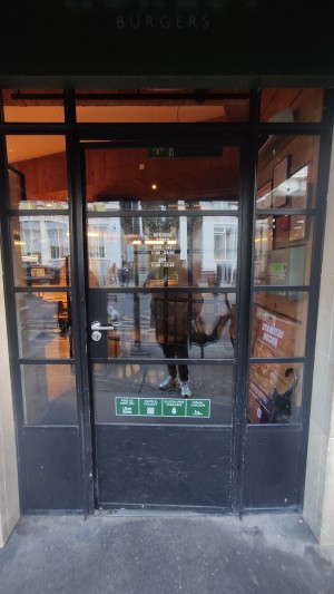 Glass door with black frames ahead. Push metal handle on left to open.