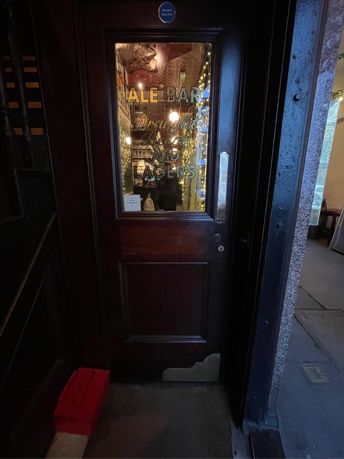 From after archway, facing right. Wood-panelled glass door ahead. Push golden, metal pad on right to open