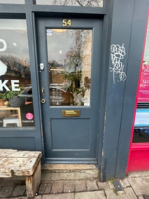 Grey wooden and glass door ahead. Push gold metal handle on left to open.