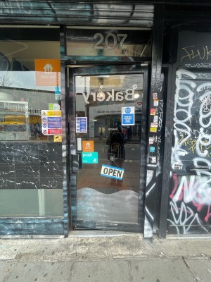 Glass door with black frame ahead. Push black metal handle on left to open.