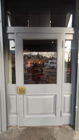 Grey door with glass panel ahead. Pull brass handle on left to open.