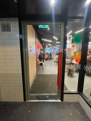 Glass door with grey frame ahead. Push red handle on right to open.