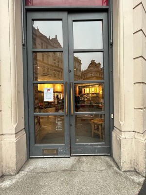 Glass doors with grey frames ahead. Push brass handles in centre to open. Doormat after.