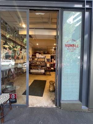 Glass door with grey metal frame. Turn silver handle and push from left to open. Doorstop obstructing on right.