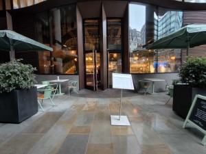 From street facing venue. Planters on left and right. Standing sign ahead. Main entrance behind.
