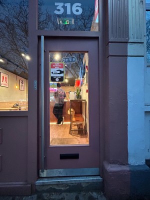 Glass door with pink wooden frame ahead. Push silver handle on left to open.