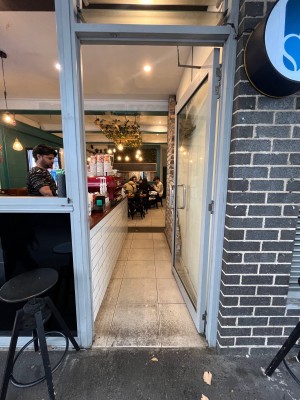 Glass door with white frame ahead. Push silver metal handle on left to open.