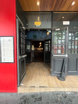 Glass double doors with black wooden frame. Doors open from inside and propped open when venue open.