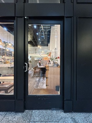 Glass door with black frame ahead. Push silver handle on left to open.
