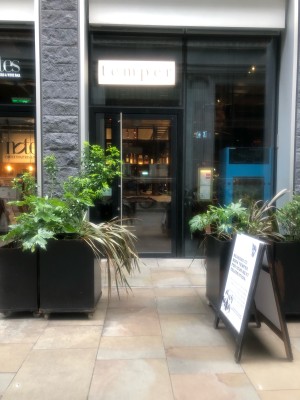 From street facing venue. Opening ahead, planters along left and right. Doors at back.
