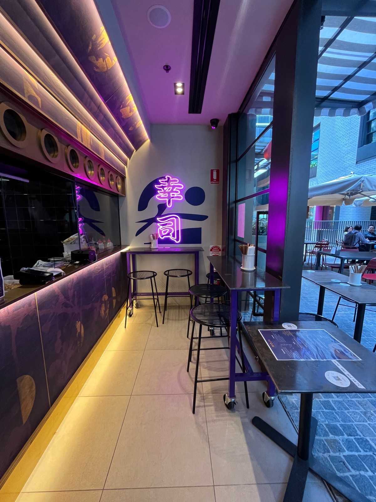 From counter facing right. Service counter on left wall. High tables with backless stools on wall ahead and on right wall ahead.