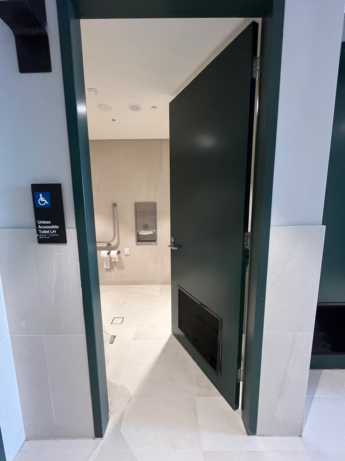 From end of hallway facing right. Dark green wooden door. Turn silver handle and push from left.