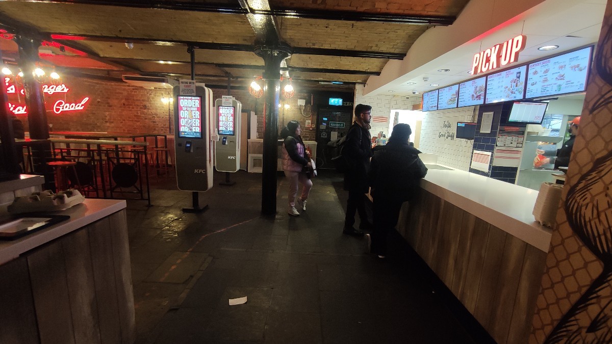 From opening facing straight. Bins on left. Self ordering screens on back left. Counter along right.