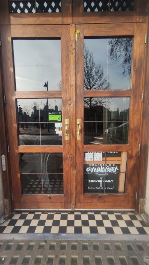 Glass doors with brown frames ahead. Pull gold handles in centre to open. Button for assistance on left of doors.