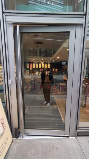 Glass door with grey frames. Push metal handle on left to open.