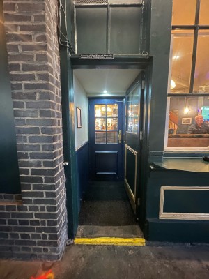 Black glass and wooden door ahead. Push gold metal handle on left to open.