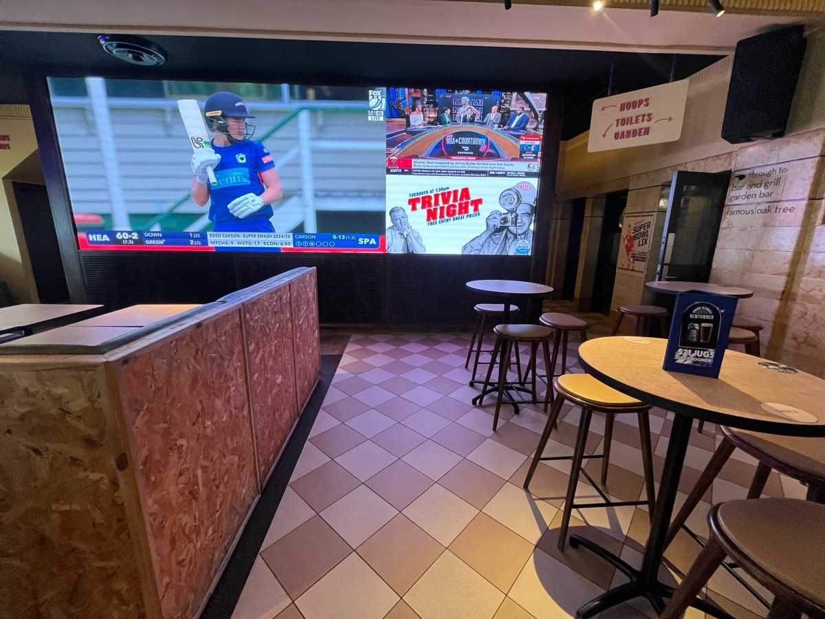 From end of bar facing straight. High tables and backless stools scattered to right.