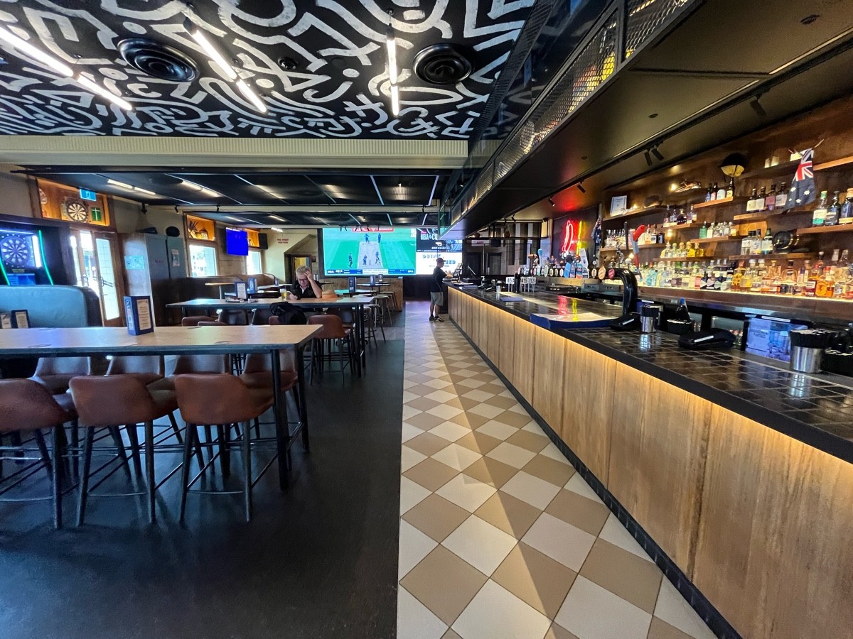 From after bar stools facing straight. High tables and backed stools along left. Bar along right.