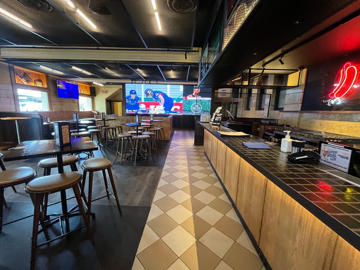 From after tables and backed stools facing straight. High tables and backless stools along left. Bar along right.