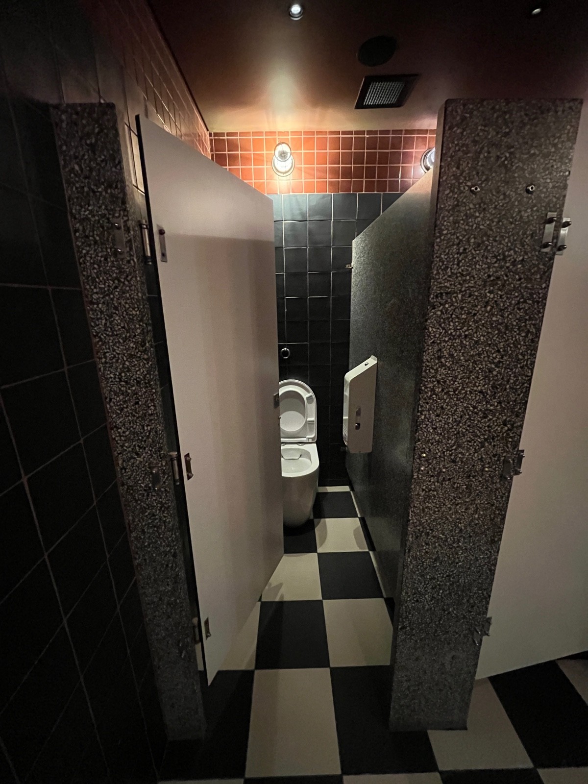 From end of urinals facing right. White wooden cubicle door. Push from right. Toilet on wall directly ahead.